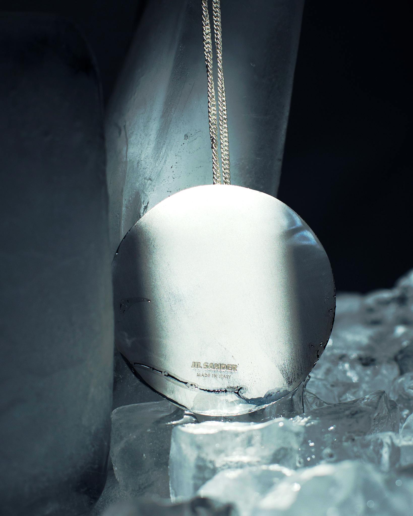 Close-up of a shiny silver pendant among ice, exuding purity and elegance.